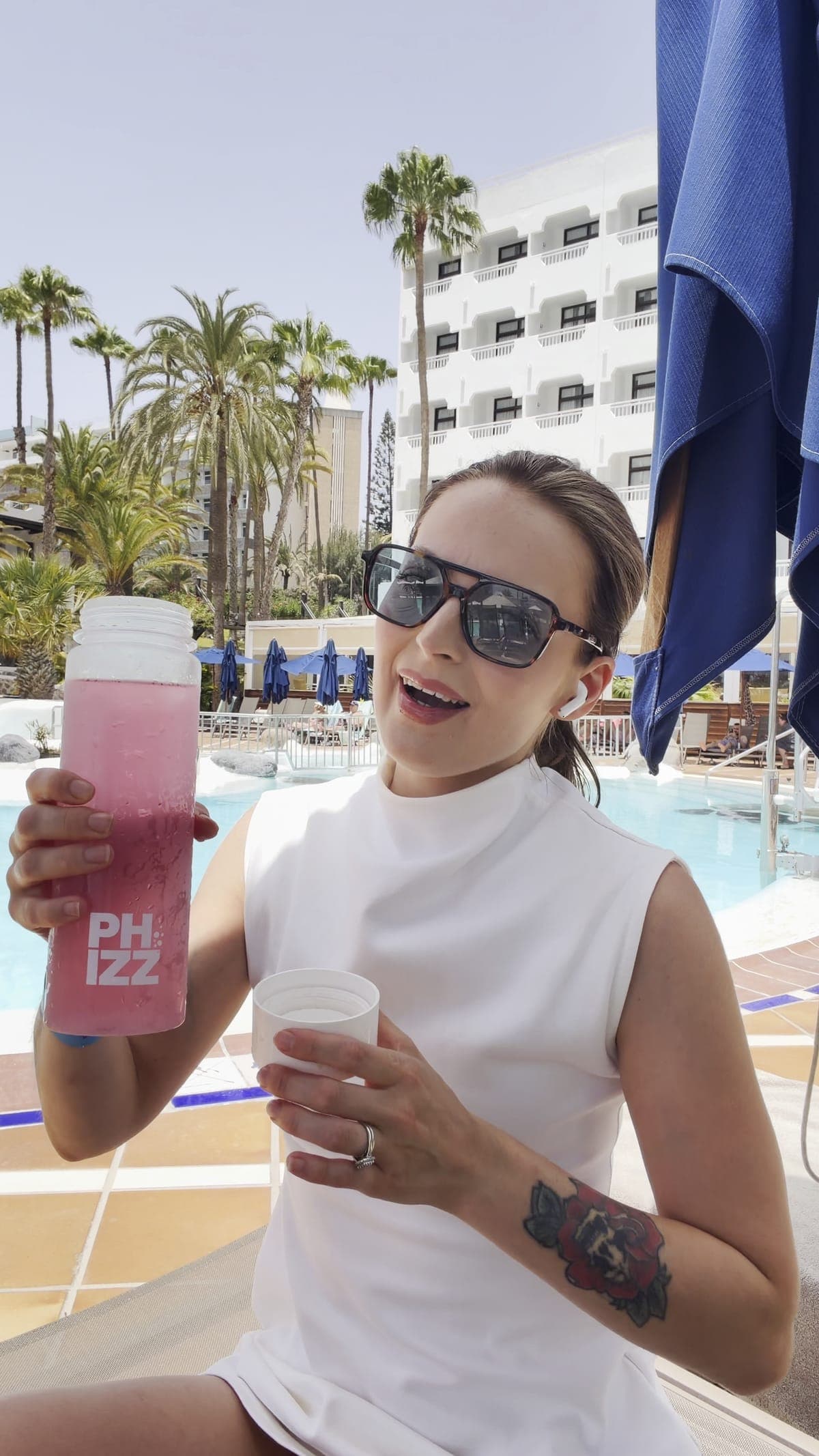 A creator by a pool chatting to camera with a pink Phizz bottle