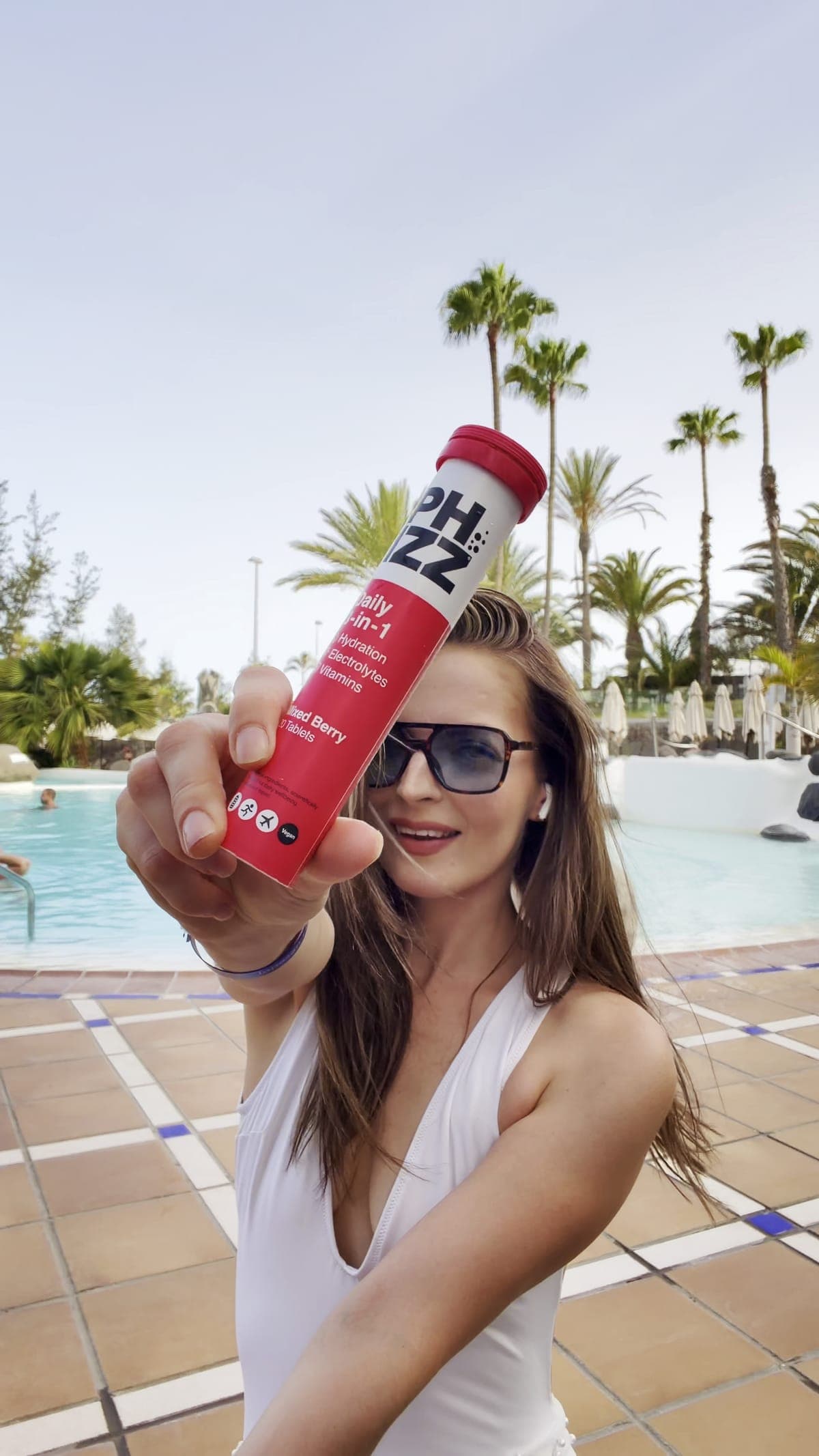 A creator by a pool holding a tube of Phizz tablets out to the camera