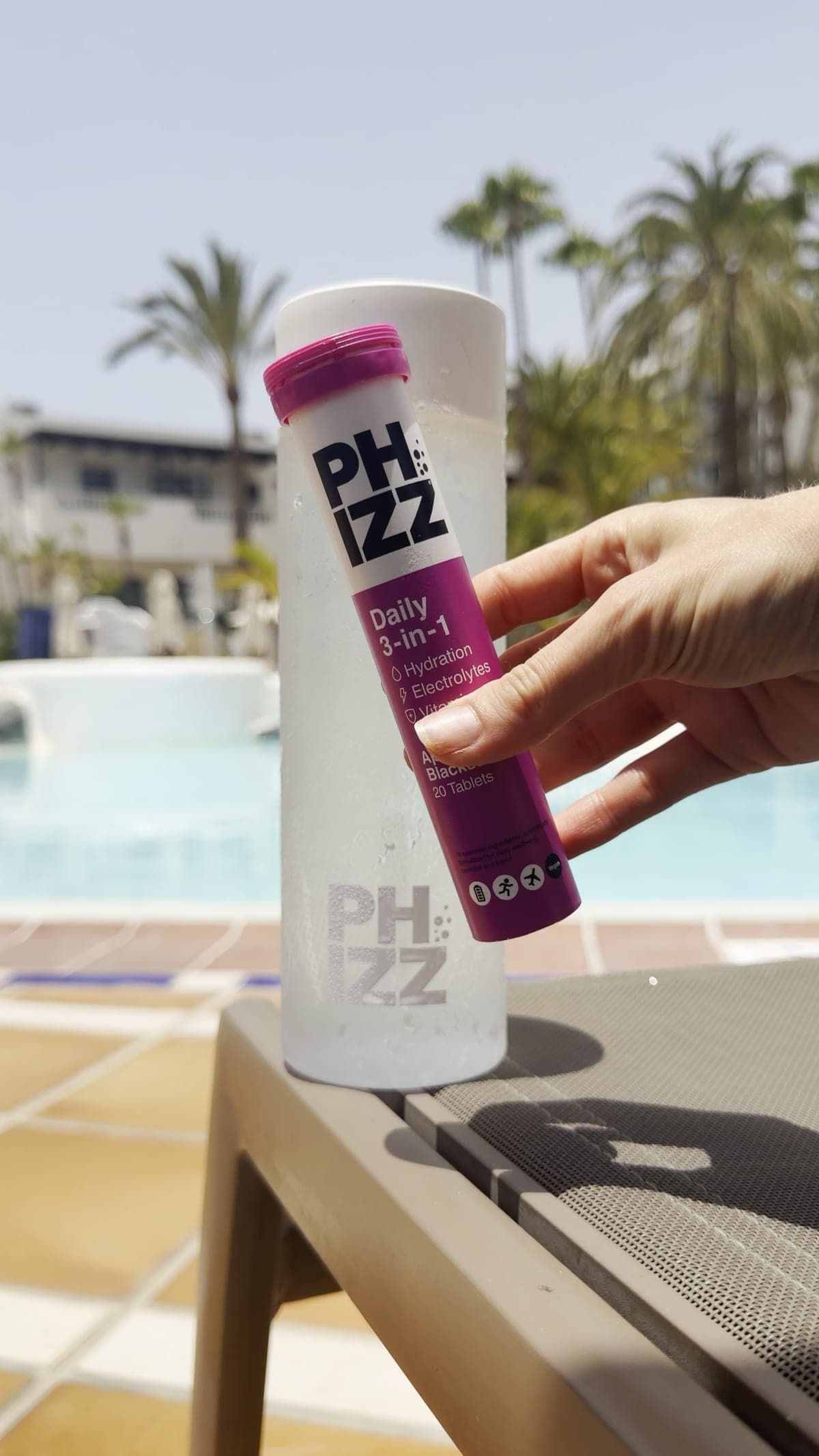 A hand holding a tube of Phizz tablets beside a bottle at a poolside table